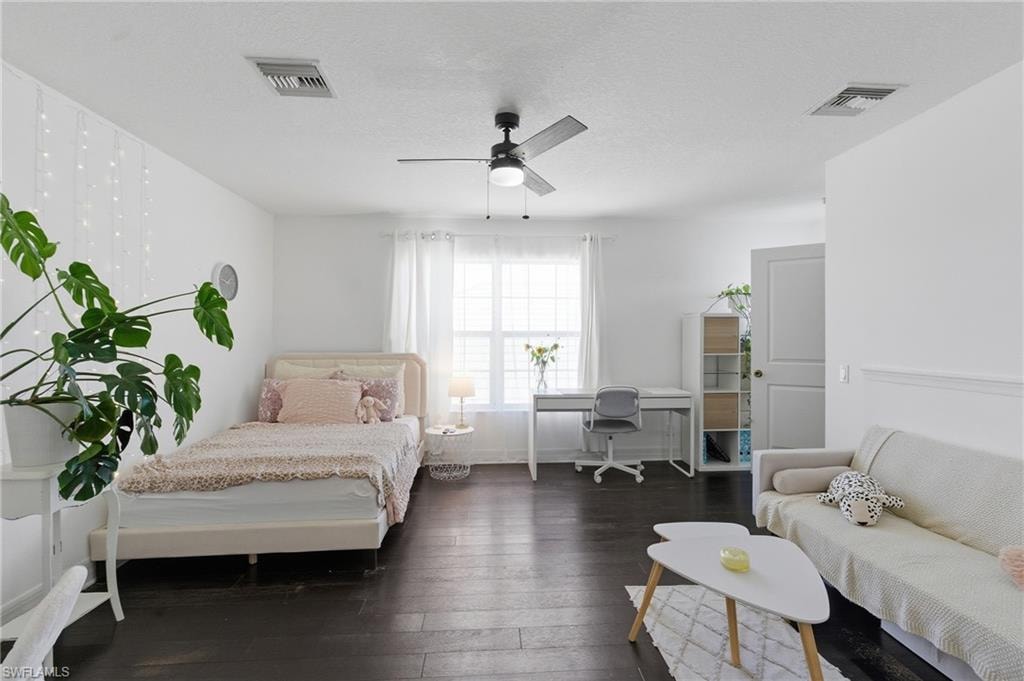 Bedroom with dark wood-type flooring, a desk, ceiling fan, and a textured ceiling