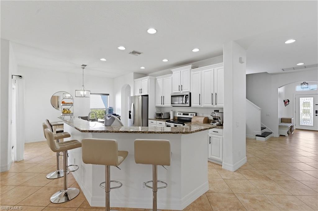 Kitchen with arched walkways, white cabinetry, dark stone counters, decorative light fixtures, and a kitchen breakfast bar