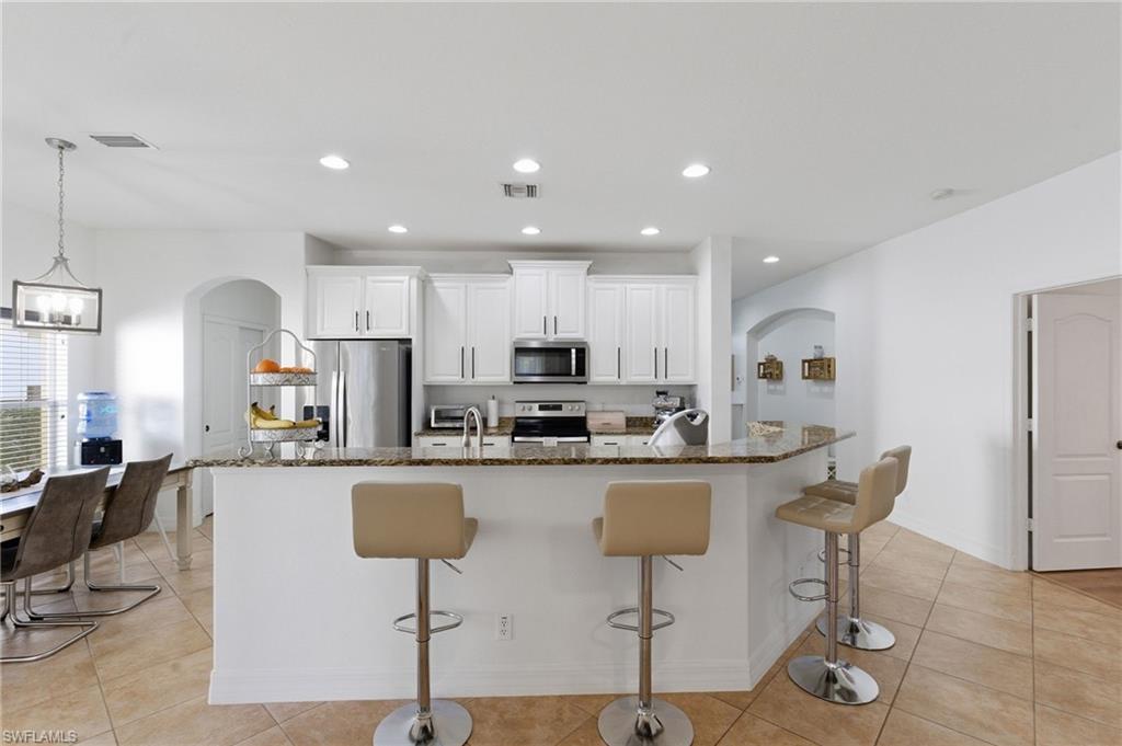 Kitchen featuring arched walkways, white cabinets, a kitchen breakfast bar, and dark stone countertops