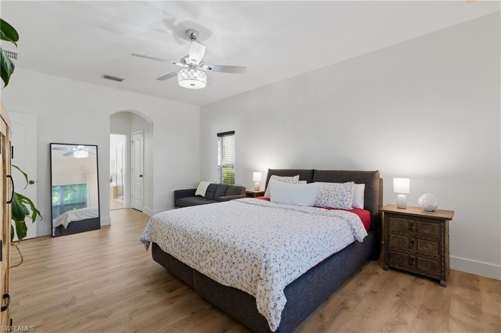 Bedroom with light wood-style flooring, arched walkways, a ceiling fan, and ensuite bath