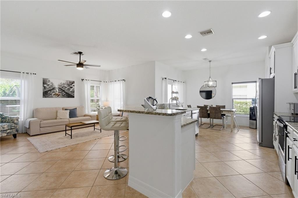Kitchen featuring a kitchen breakfast bar, white cabinetry, light stone countertops, and light tile patterned flooring