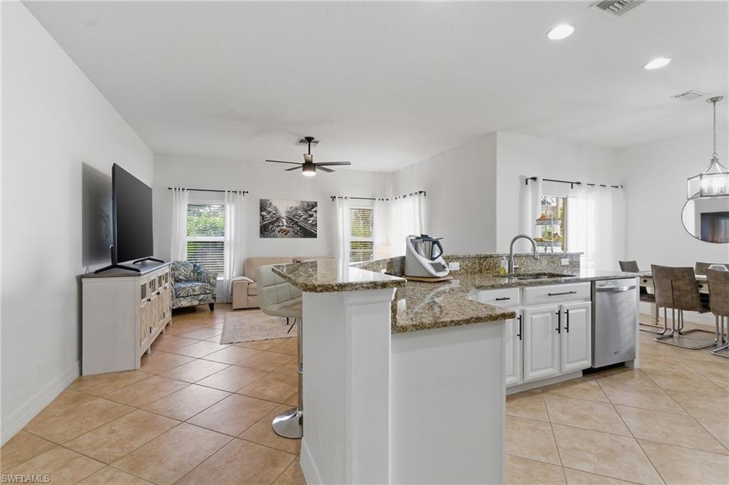 Kitchen with white cabinets, light stone counters, an island with sink, and light tile patterned floors