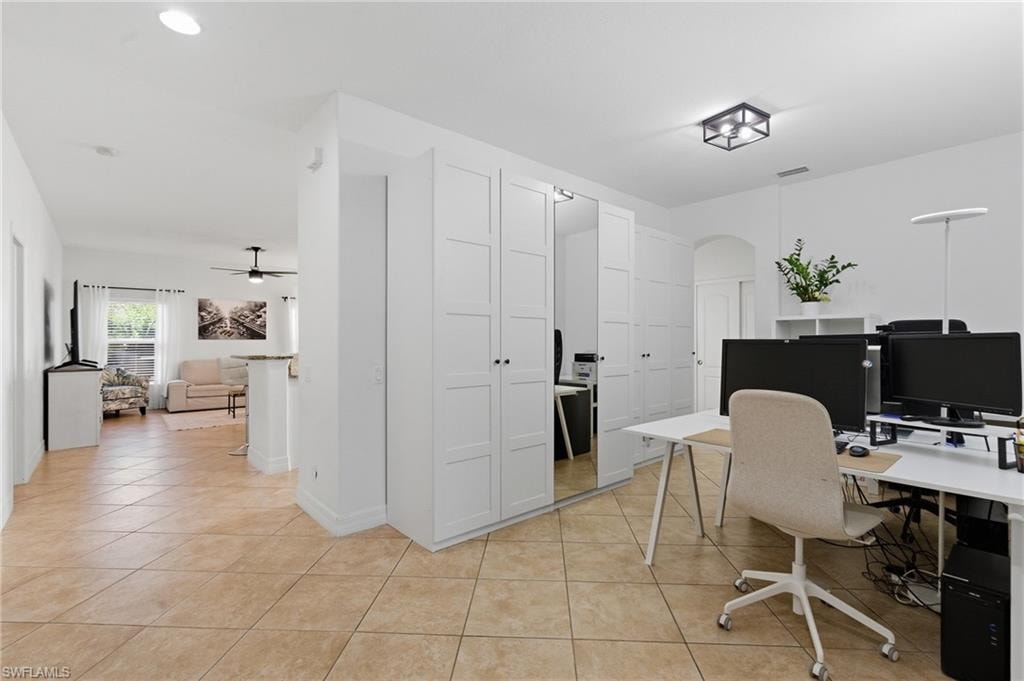 Home office with arched walkways, light tile patterned floors, and a ceiling fan