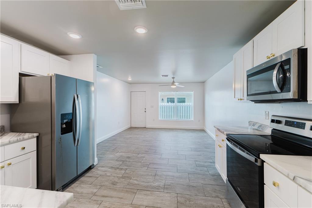 Kitchen with stainless steel appliances, white cabinetry, light stone countertops, a ceiling fan, and recessed lighting