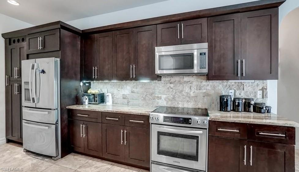 Kitchen featuring stainless steel appliances, light stone countertops, and dark wood finish cabinets