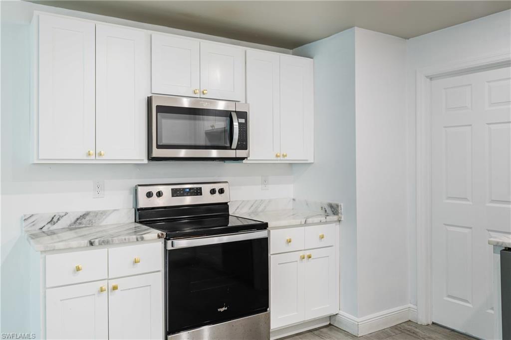 Kitchen with stainless steel appliances, white cabinets, and light stone countertops