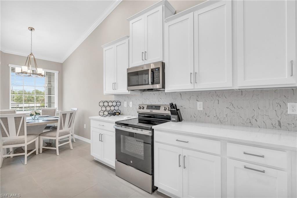 Kitchen featuring lofted ceiling, decorative backsplash, light tile patterned floors, appliances with stainless steel finishes, and white cabinets