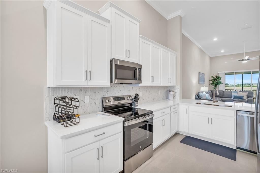 Kitchen with appliances with stainless steel finishes, white cabinets, backsplash, and sink