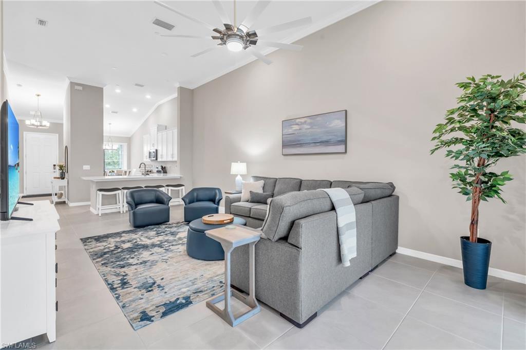 Living room featuring vaulted ceiling, sink, crown molding, light tile patterned floors, and ceiling fan with notable chandelier