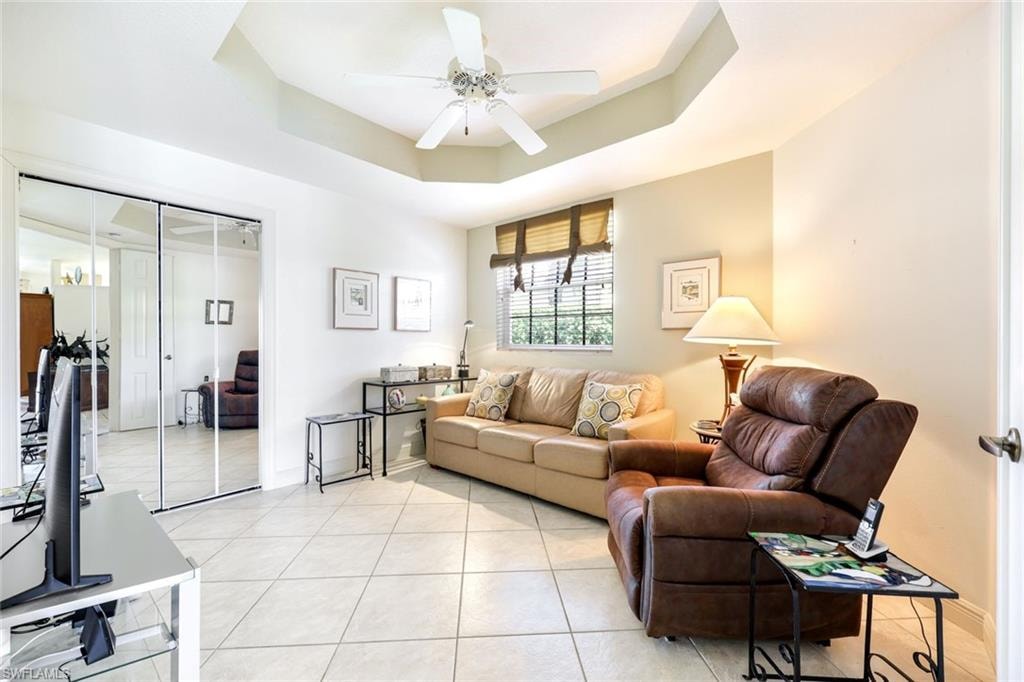 Living area with ceiling fan, a raised ceiling, and light tile patterned floors