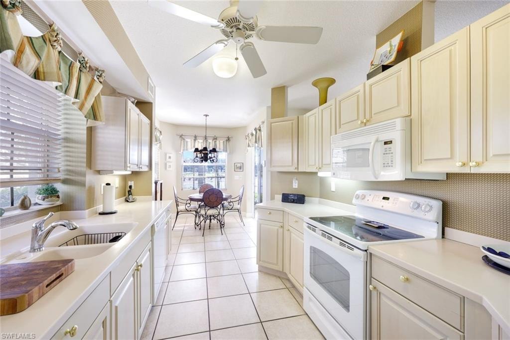 Kitchen featuring white appliances, light countertops, ceiling fan, light tile patterned flooring, and hanging light fixtures