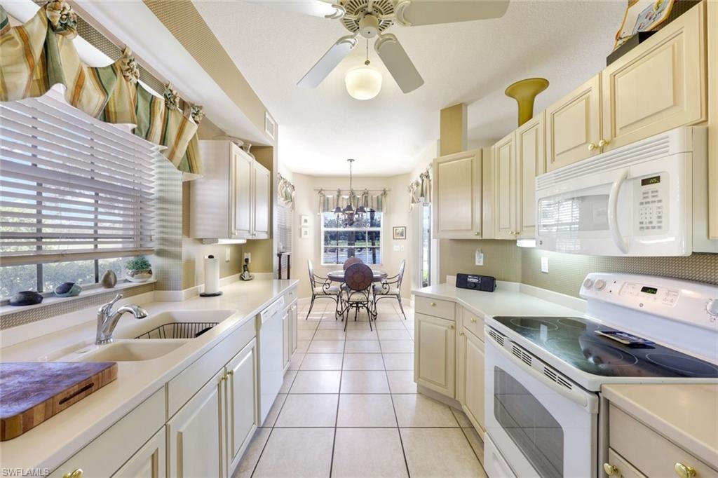 Kitchen with white appliances, light countertops, ceiling fan, light tile patterned flooring, and pendant lighting