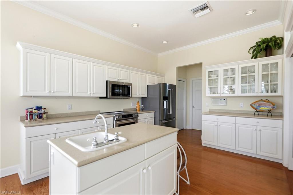 Kitchen featuring white cabinets, light countertops, stainless steel appliances, glass insert cabinets, and dark wood-style flooring