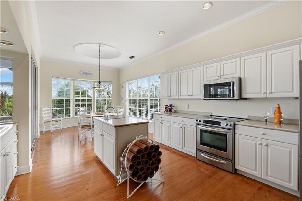 Kitchen with white cabinetry, stainless steel appliances, crown molding, an island with sink, and light wood finished floors