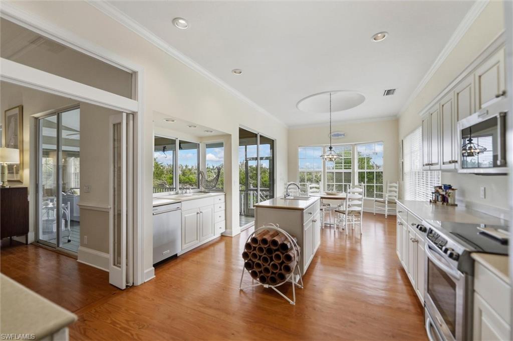 Kitchen featuring stainless steel appliances, crown molding, a kitchen island with sink, hanging light fixtures, and light wood-style flooring