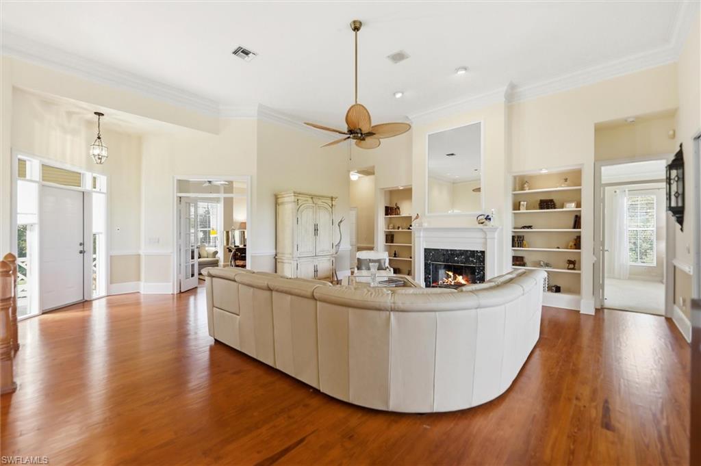 Living area with a ceiling fan, crown molding, wood finished floors, a fireplace, and built in features