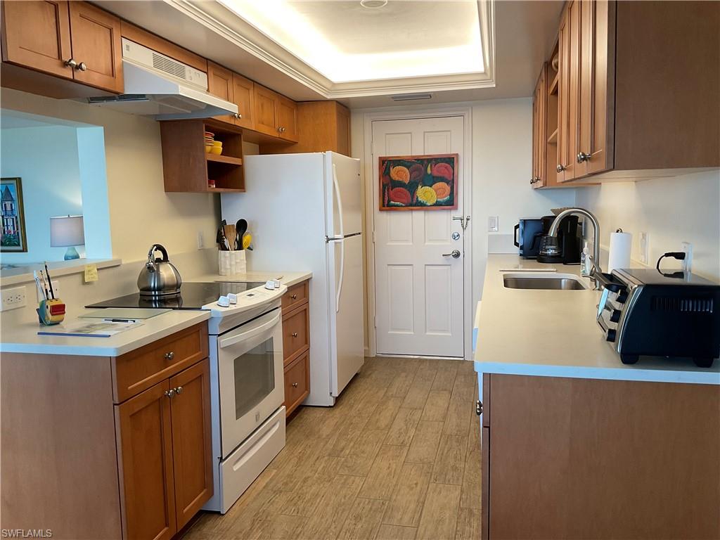 Kitchen with white electric stove, under cabinet range hood, brown cabinetry, and a sink
