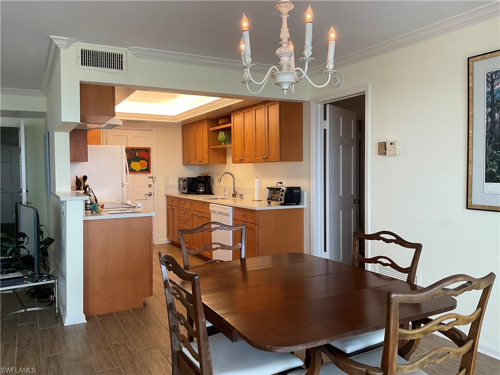 Dining room with wood finish floors, visible vents, a notable chandelier, ornamental molding, and a raised ceiling