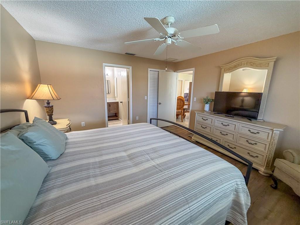 Bedroom with a textured ceiling, dark wood-style flooring, a ceiling fan, and connected bathroom