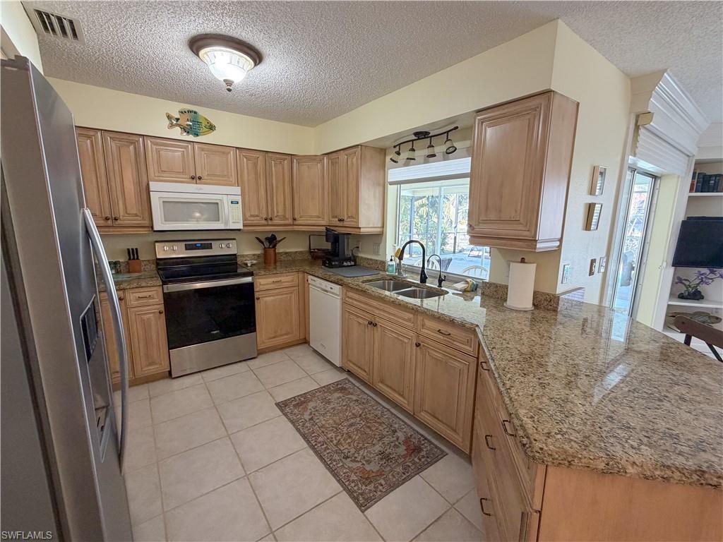 Kitchen featuring stainless steel appliances, a textured ceiling, light stone counters, a peninsula, and light tile patterned floors