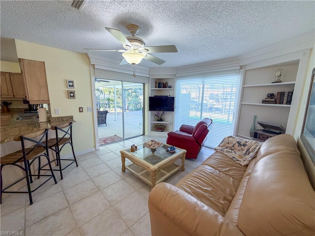 Living room with built in shelves, a textured ceiling, light tile patterned flooring, and a ceiling fan