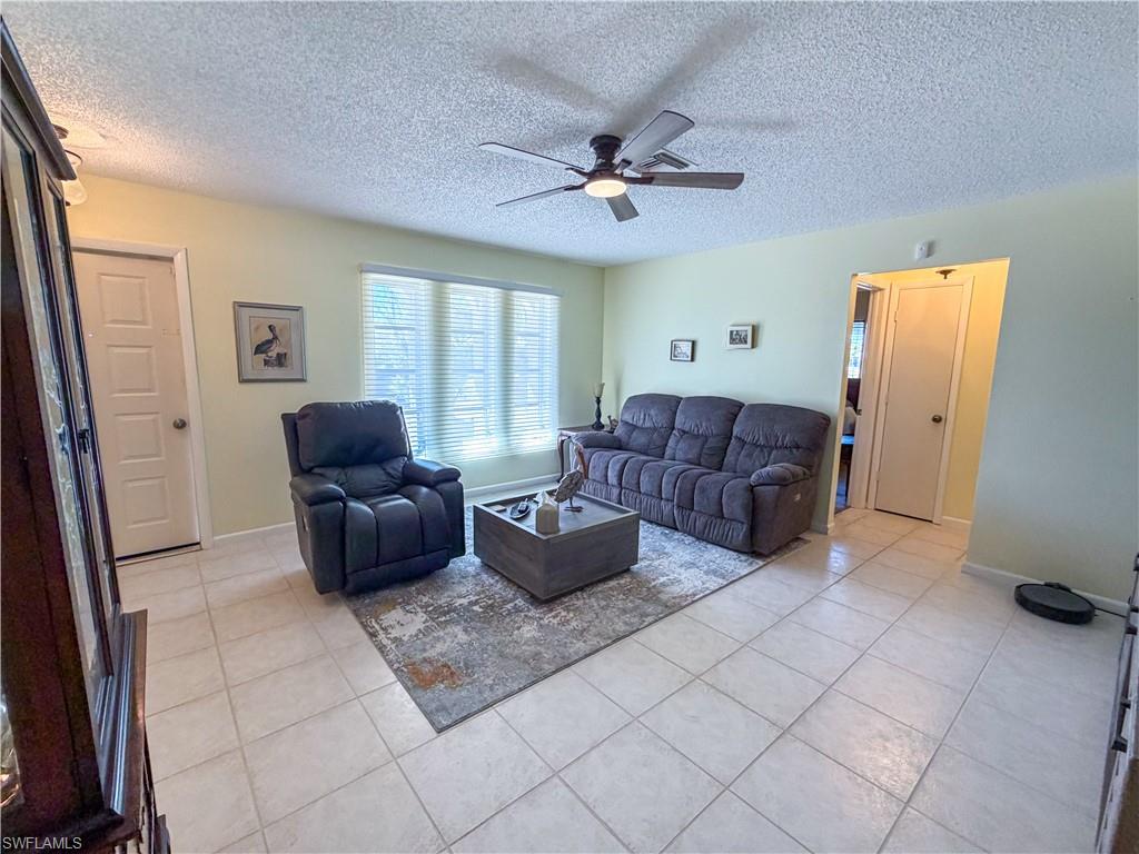 Living area featuring a ceiling fan, light tile patterned flooring, and a textured ceiling