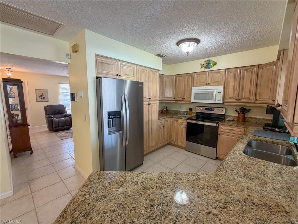 Kitchen featuring stainless steel appliances, light tile patterned floors, light stone countertops, and a textured ceiling