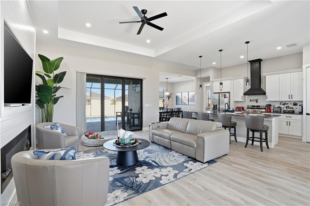 Living room with a ceiling fan, light wood finished floors, a raised ceiling, recessed lighting, and a fireplace