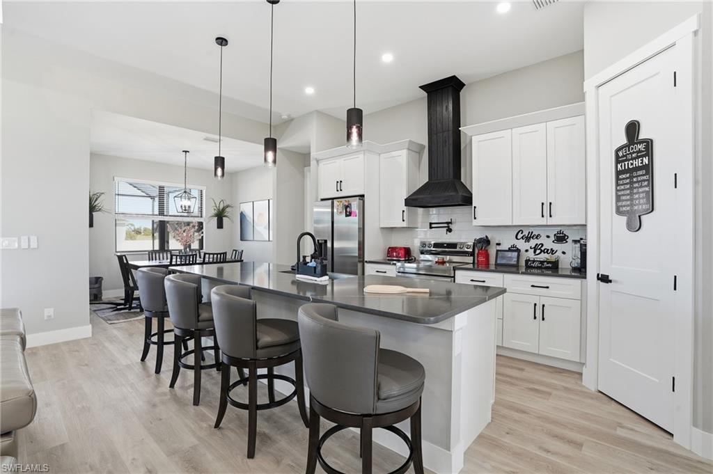 Kitchen with an island with sink, white cabinets, a breakfast bar area, stainless steel appliances, and pendant lighting