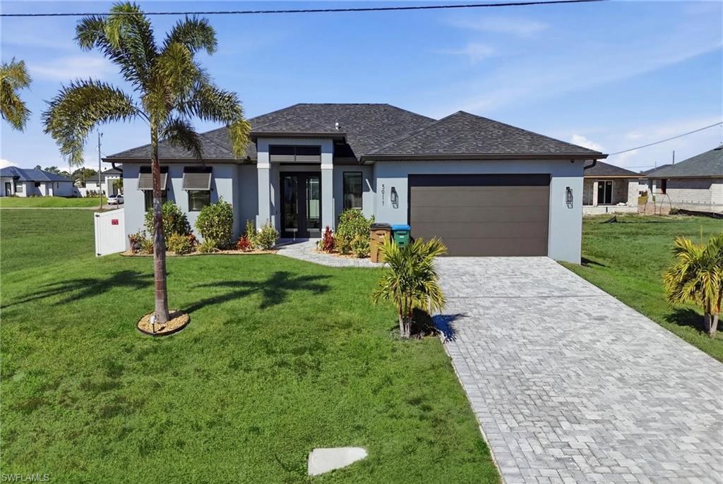 Prairie-style house with stucco siding, a front yard, decorative driveway, and a shingled roof