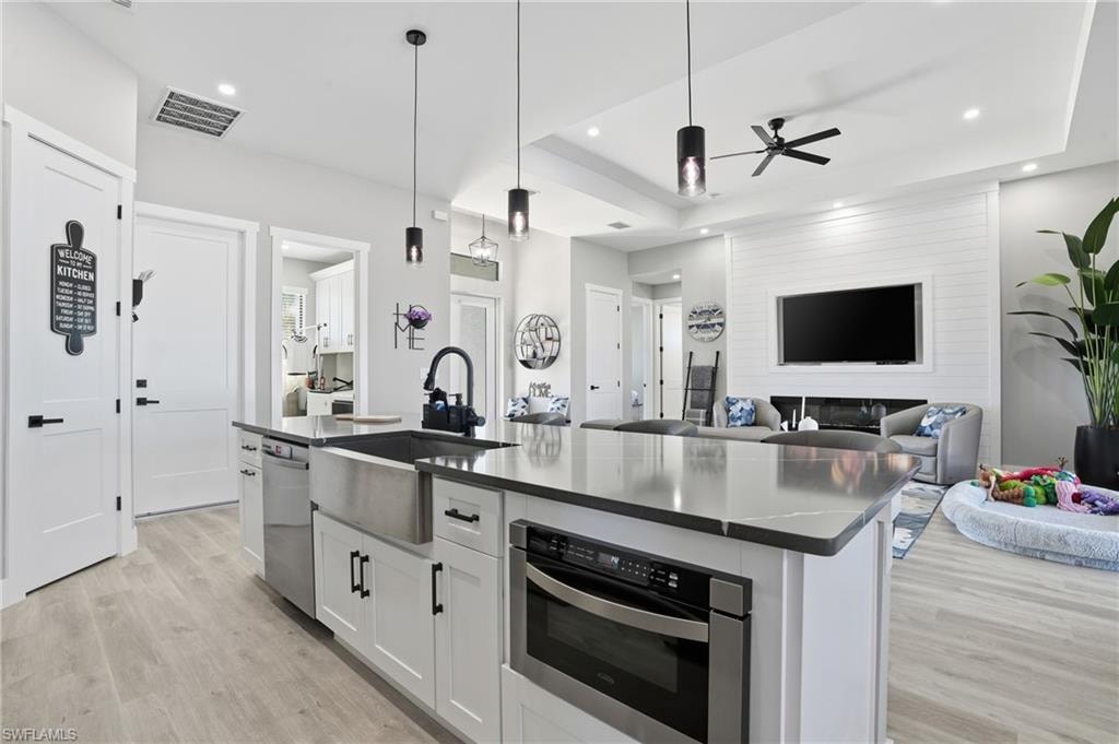 Kitchen featuring white cabinets, a kitchen island with sink, open floor plan, pendant lighting, and light wood-type flooring