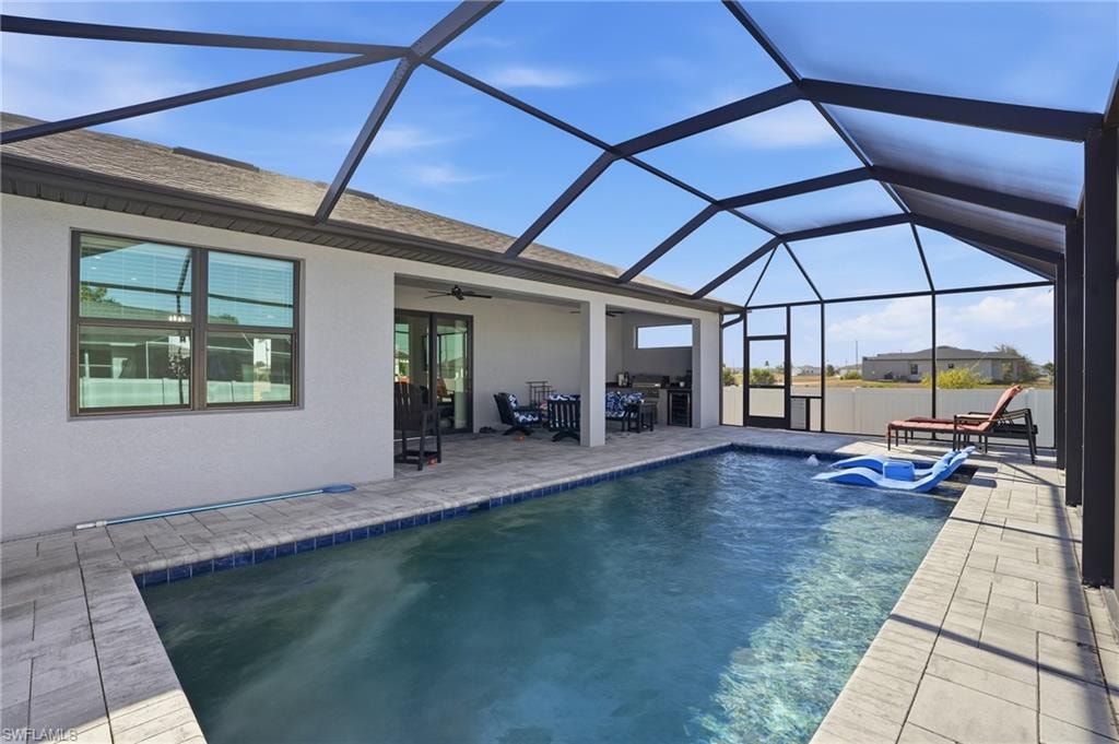 Swimming pool featuring a sunroom, a patio, glass enclosure, and an outdoor kitchen