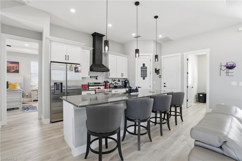 Kitchen featuring white cabinetry, stainless steel appliances, a kitchen bar, light wood-style flooring, and an island with sink