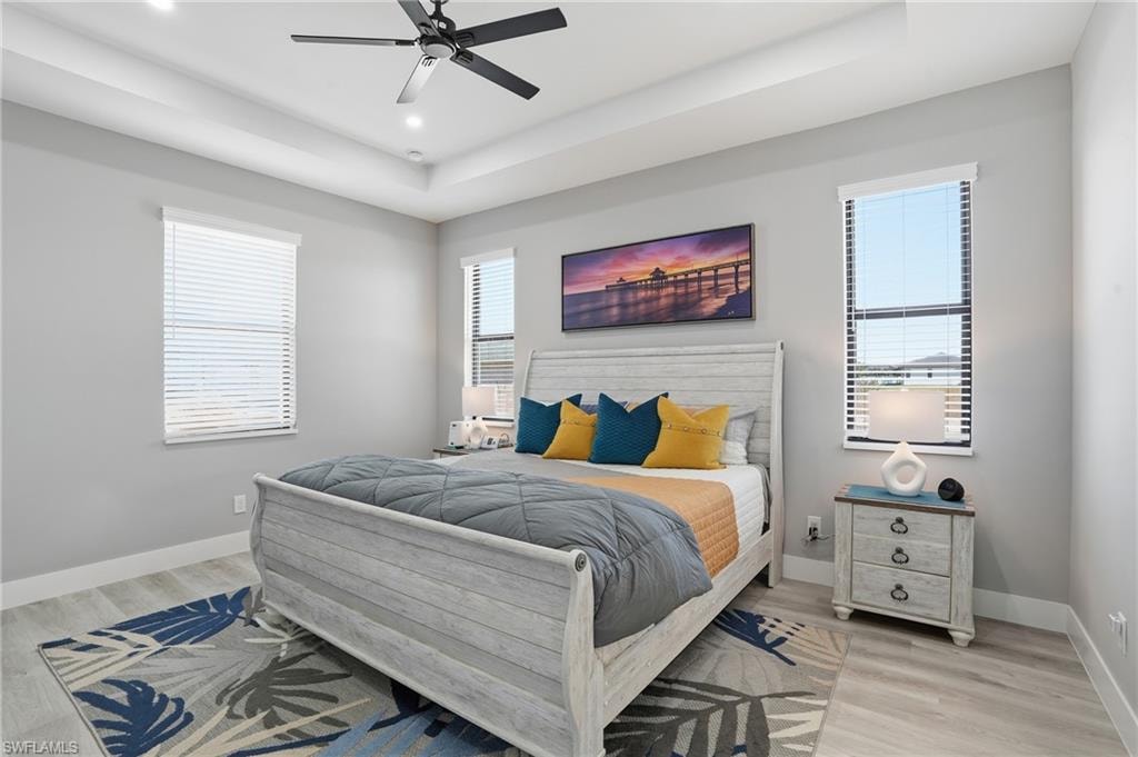 Bedroom with a raised ceiling, light wood-type flooring, and a ceiling fan