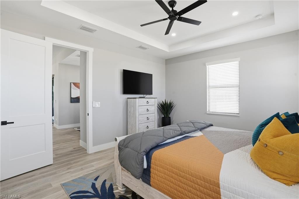 Bedroom with a tray ceiling, light wood finished floors, ceiling fan, and recessed lighting