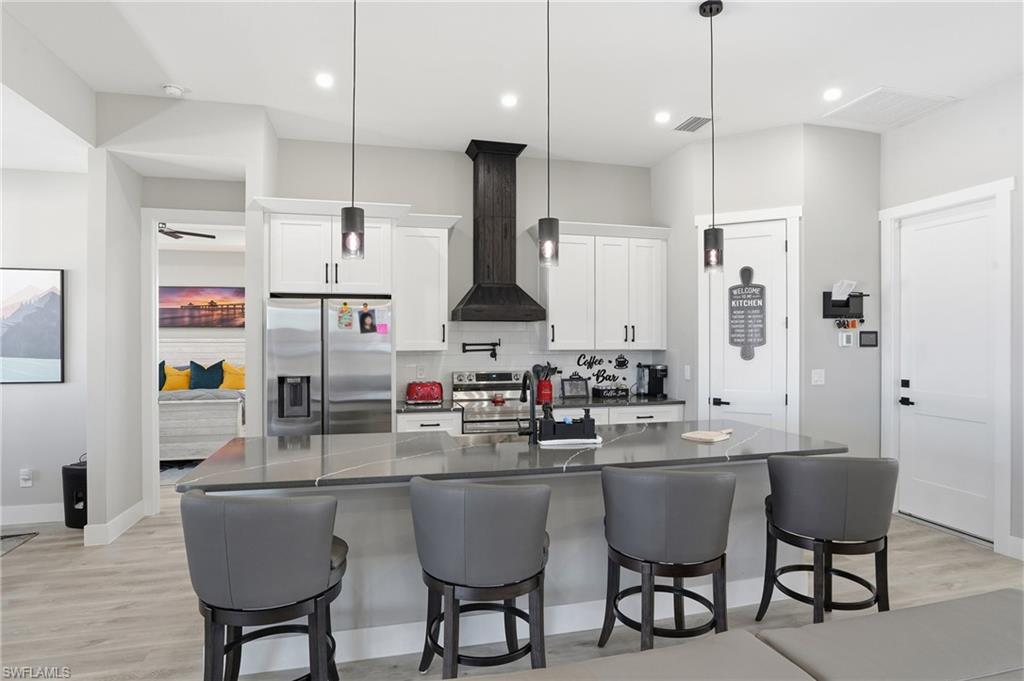 Kitchen with white cabinetry, stainless steel appliances, light wood-style floors, a kitchen breakfast bar, and tasteful backsplash