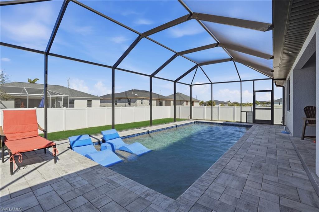 View of swimming pool with a sunroom, glass enclosure, a fenced backyard, patio surround, and a residential view
