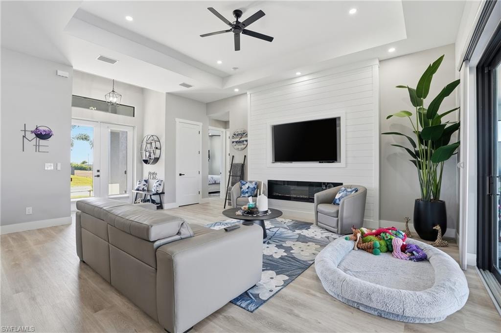 Living area featuring a ceiling fan, light wood finished floors, a raised ceiling, a glass covered fireplace, and recessed lighting