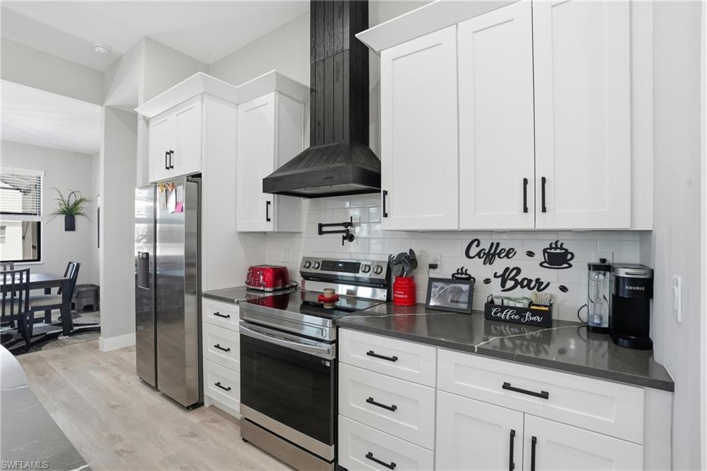 Kitchen featuring stainless steel appliances, backsplash, white cabinets, light wood-type flooring, and dark stone countertops