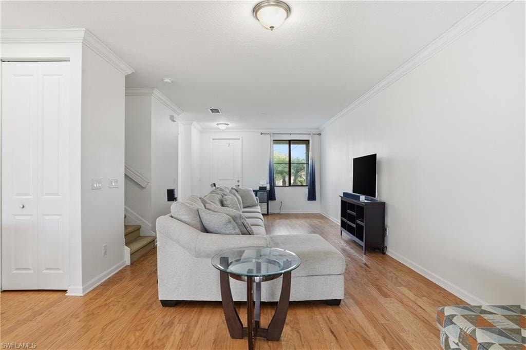 Living room with crown molding, stairway, and light wood finished floors
