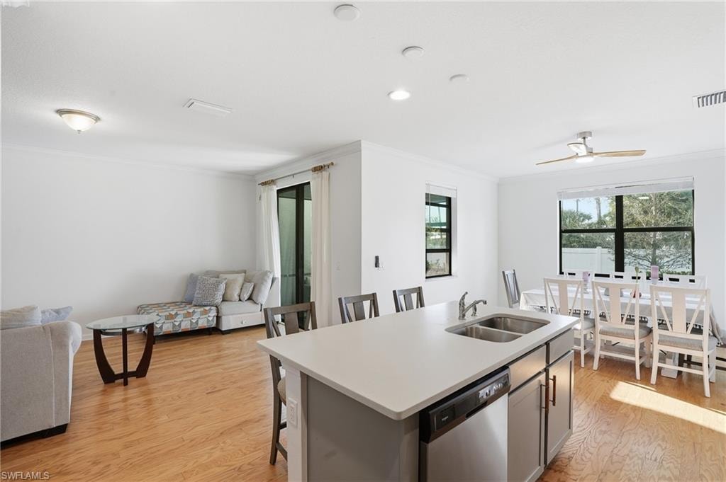 Kitchen with light countertops, an island with sink, a kitchen bar, light wood-style flooring, and dishwasher