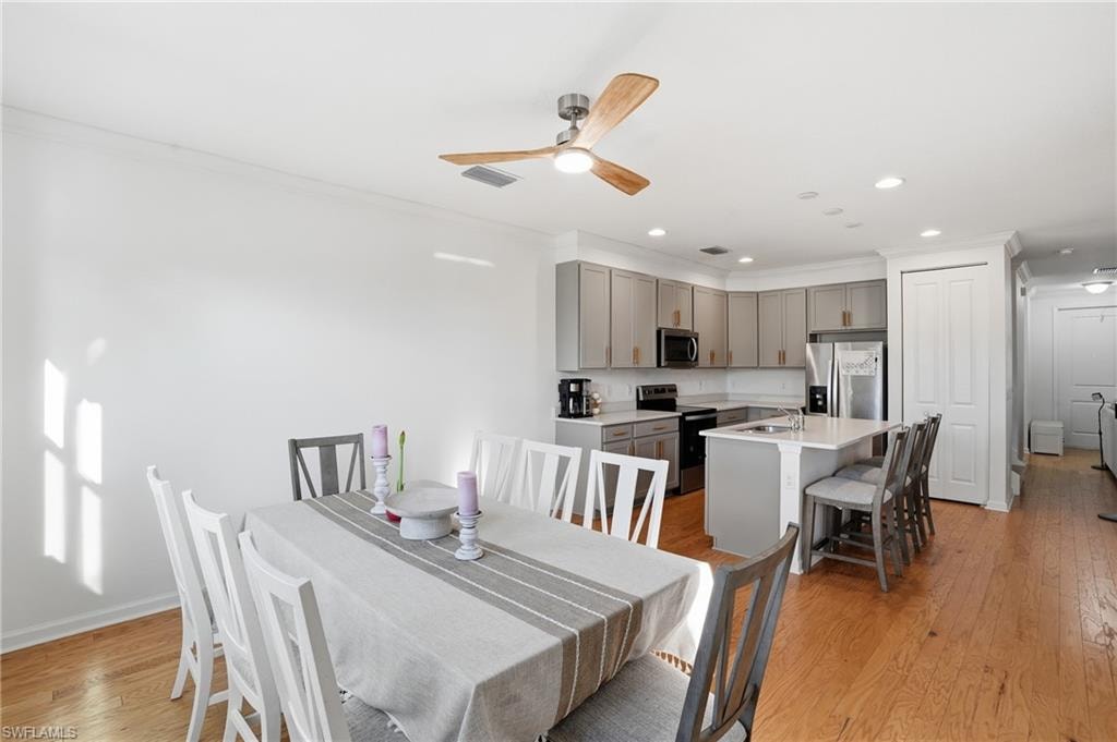 Dining area with light wood-style floors, crown molding, a ceiling fan, and recessed lighting