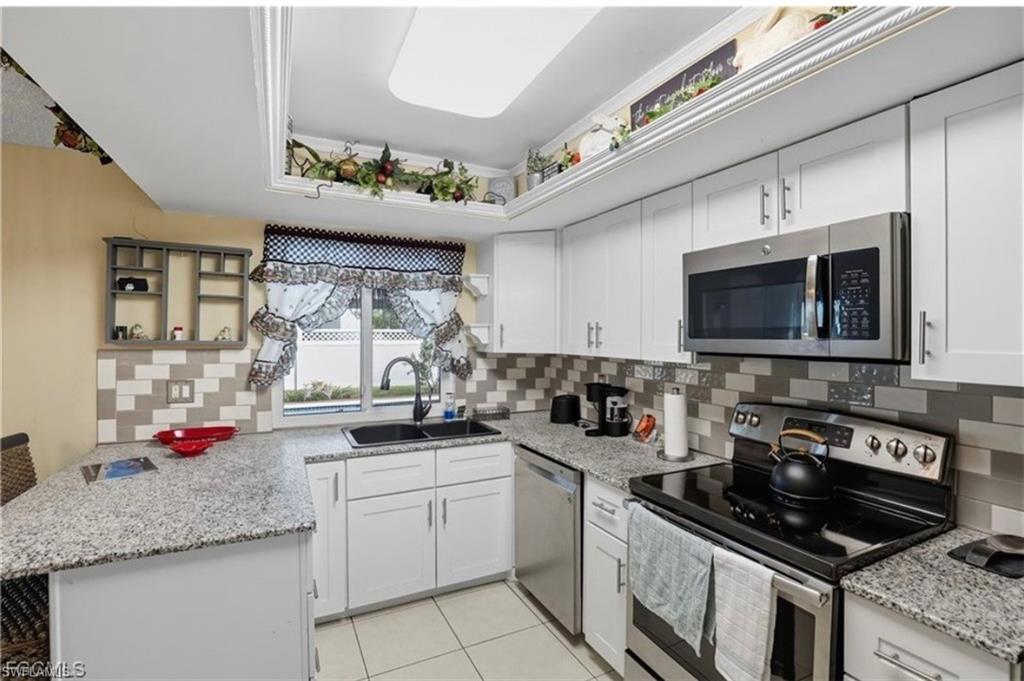 Kitchen featuring stainless steel appliances, open shelves, light stone counters, and white cabinetry