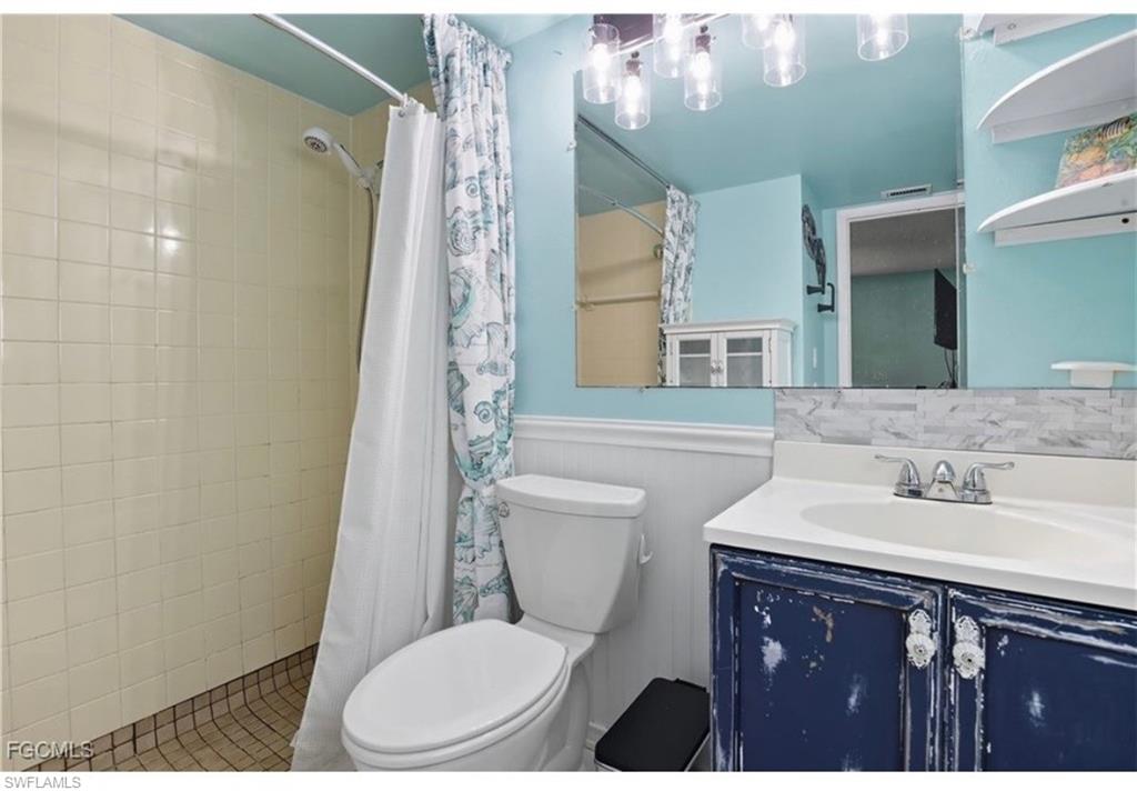 Full bath featuring vanity, wainscoting, and tiled shower