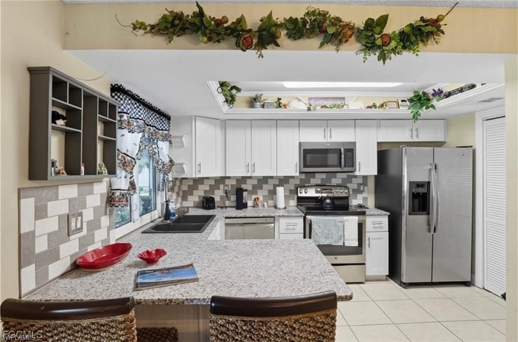 Kitchen featuring stainless steel appliances, backsplash, a peninsula, light stone countertops, and white cabinets
