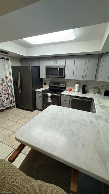 Kitchen with gray cabinets, stainless steel appliances, light stone counters, and backsplash