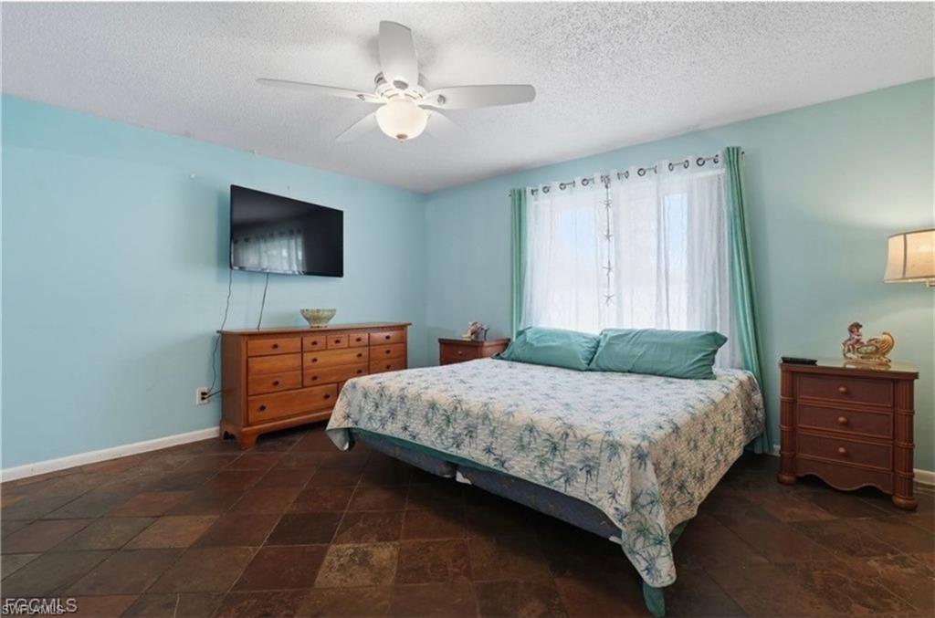 Bedroom with dark stone finish floors, ceiling fan, and a textured ceiling