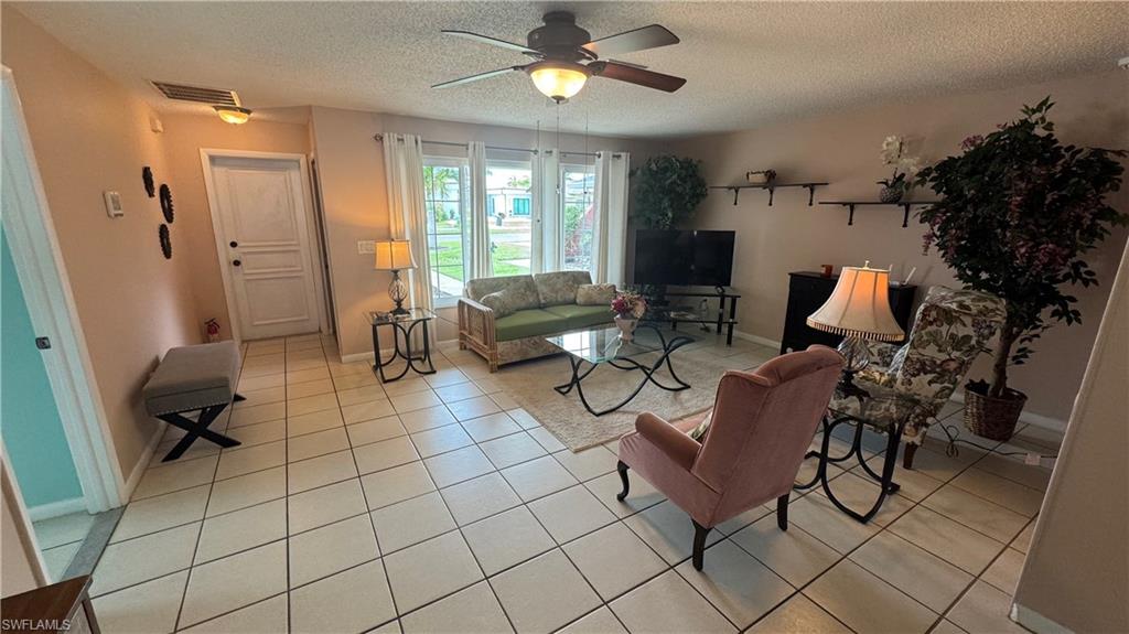 Living area featuring a ceiling fan, light tile patterned flooring, and a textured ceiling