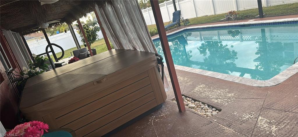 View of pool with a hot tub, a fenced backyard, and a sunroom