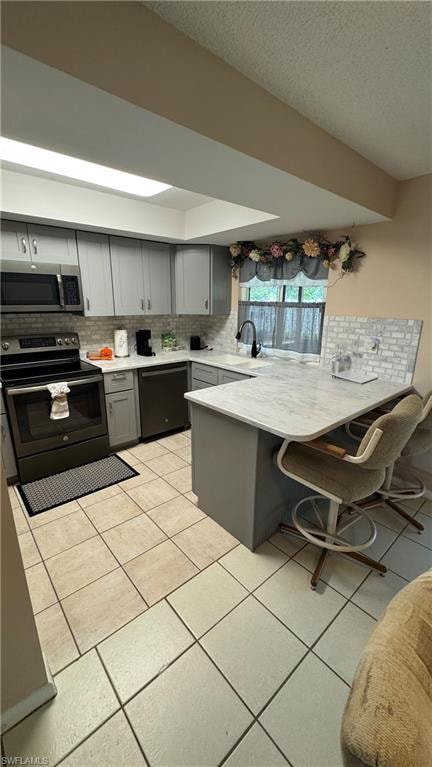 Kitchen with a breakfast bar, range with electric stovetop, gray cabinets, a peninsula, and tasteful backsplash